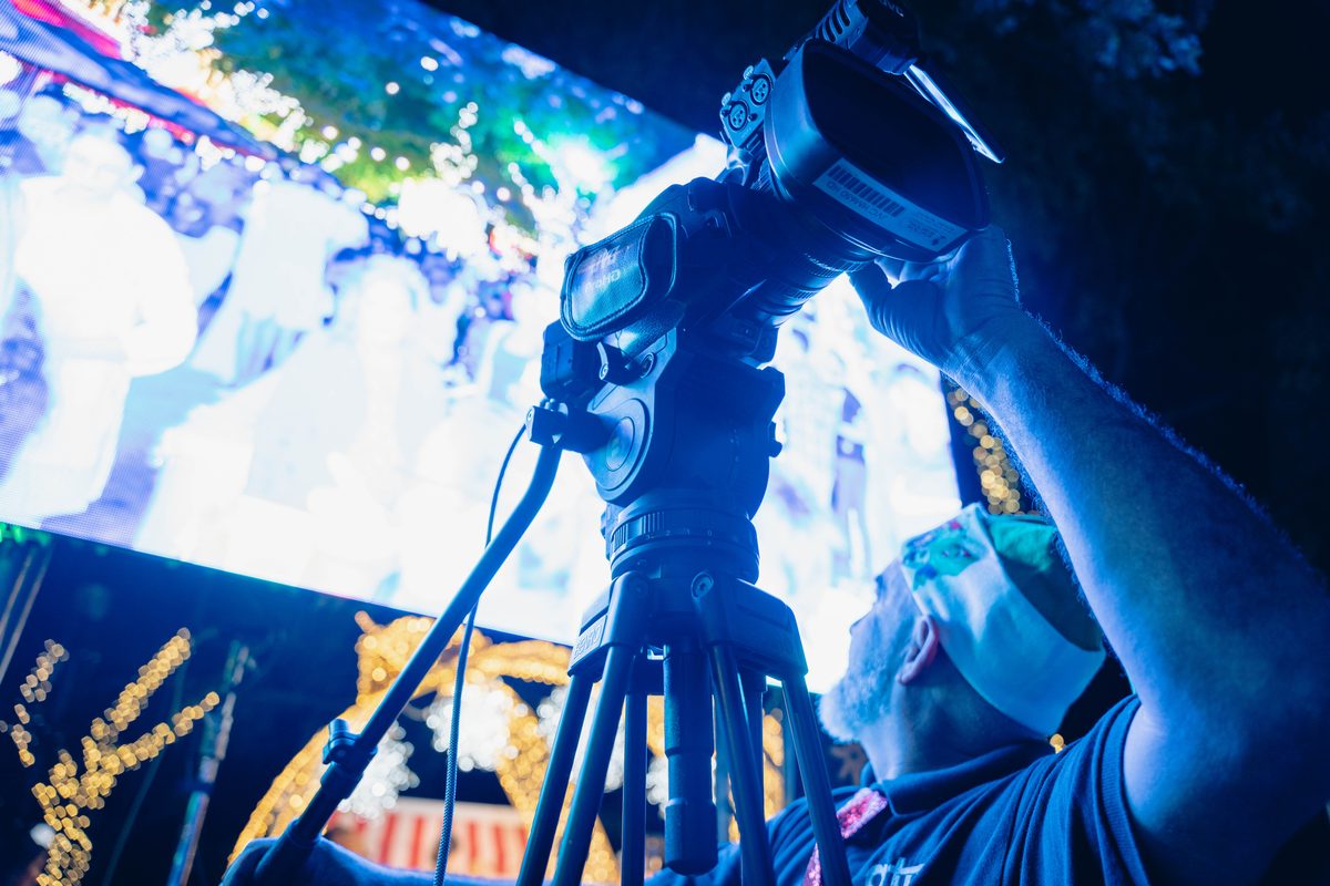 ATM camera operator running a broadcast camcorder on a fluid-head tripod