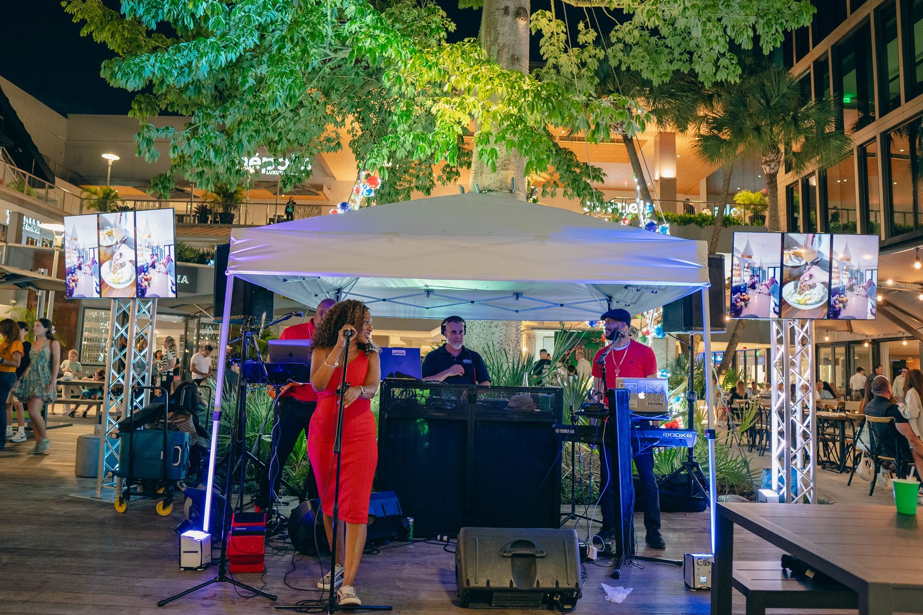 Stage at the Coconut Grove Tree Lighting with a live band, LED screens on truss towers, PA speakers and blue uplighting